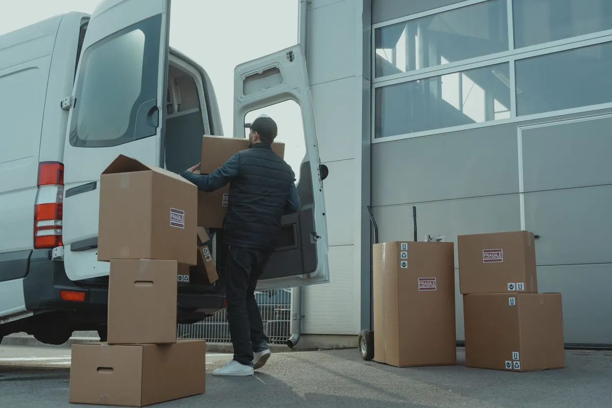 Ein Helfer lädt Kartons an einer Gebäuderampe in einen Transporter