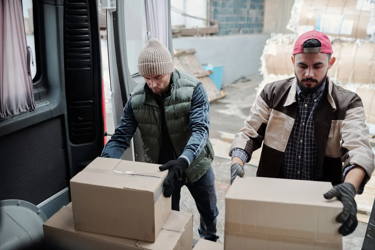 Zwei Helfer laden Kartons an einer Laderampe auf eine Sackkarre