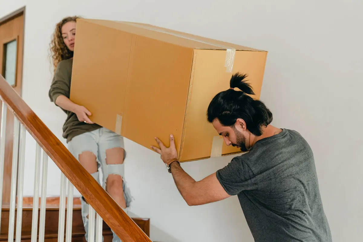 Zwei Personen tragen einen Karton über eine Innentreppe