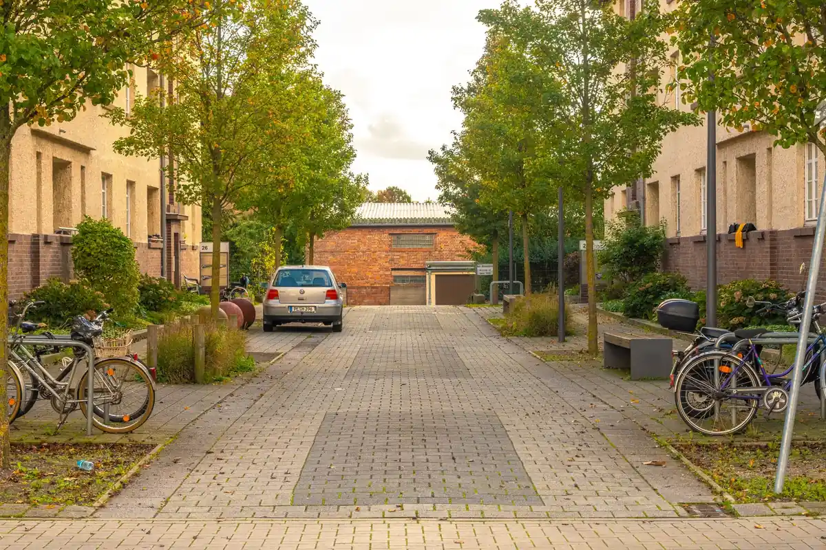 Eine schmale Wohnstraße mit Häusern, Fahrrädern und parkenden Autos