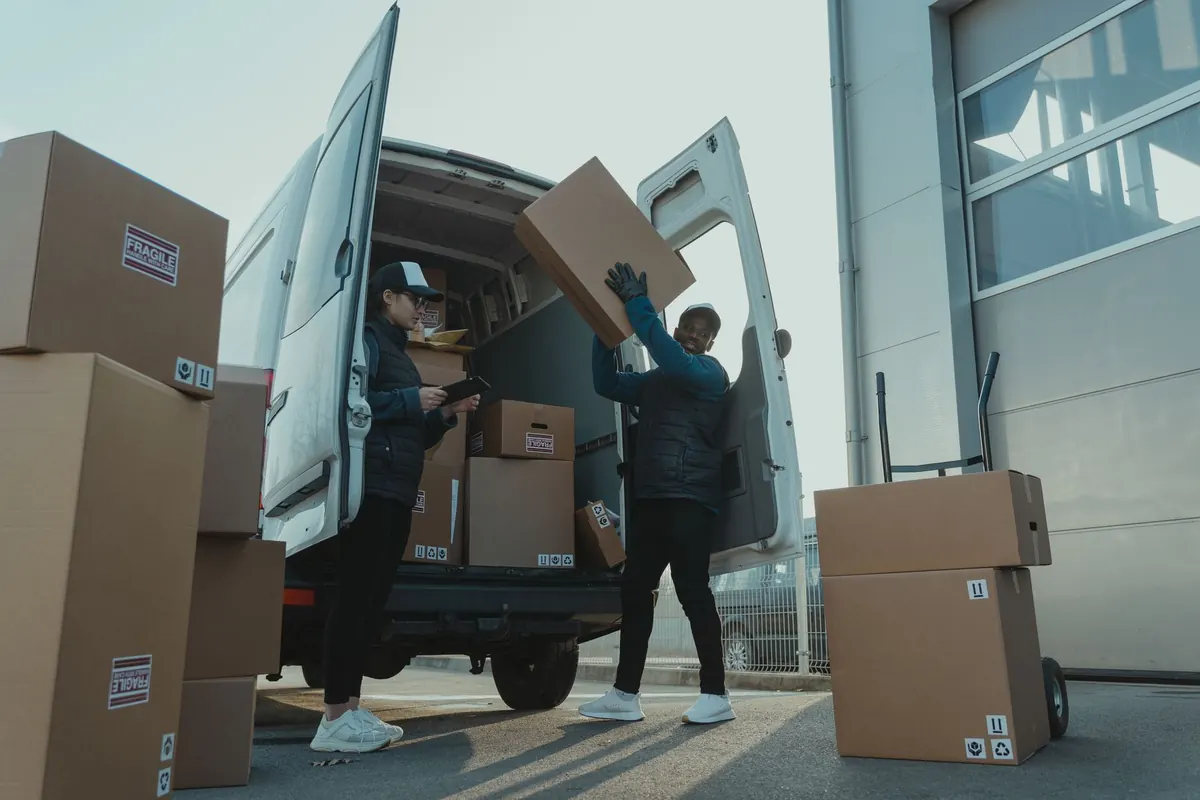 Zwei Helfer laden Kartons in einen weißen Transporter